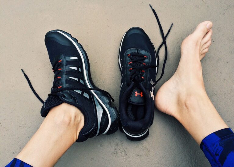 Top-down view of a person wearing dark athletic sneakers on a gray concrete surface, with a bare foot nearby and shoelaces loose on the ground.